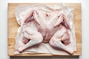 a raw spatchcocked turkey on top of a cutting board and parchment paper
