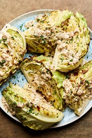 a platter of roasted cabbage wedges drizzled with mustard cream sauce and lemon juice, garnished with chives and pepper