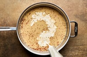 cream being added to a pan of mustard cream sauce