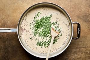 chives being stirred into a pan of mustard cream sauce