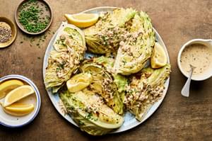 a platter of roasted cabbage wedges drizzled with mustard cream sauce and lemon juice, garnished with chives and pepper