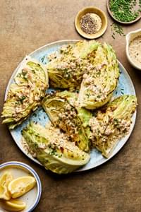 a platter of roasted cabbage wedges drizzled with mustard cream sauce and lemon juice, garnished with chives and pepper