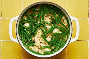 pasta and green beans being cooked in a large pot of boiling water