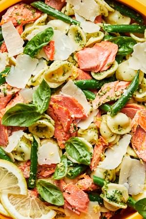 salmon pasta with homemade pesto tossed with green beans and lemon zest and sprinkled with parmesan cheese in a serving bowl