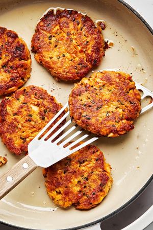 homemade salmon patties being cooked in vegetable oil in a skillet