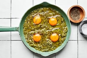 salsa verde in a skillet topped with 4 raw eggs, sprinkled with salt and pepper