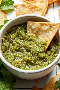 a chip being dipped into a a bowl of homemade salsa verde made with tomatillos, onion, jalapeños, cilantro and salt