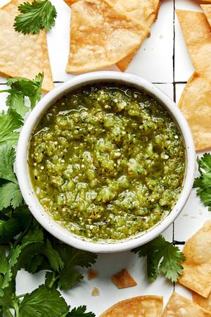 a bowl of salsa verde made with tomatillos, onion, jalapeños, cilantro and salt surrounded by tortilla chips and cilantro
