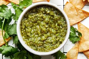a bowl of salsa verde made with tomatillos, onion, jalapeños, cilantro and salt surrounded by tortilla chips and cilantro