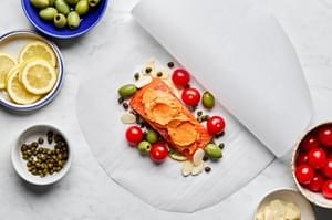 seasoned salmon fillets, lemon slices, thyme and tomato compound butter, olives and capers being wrapped in parchment