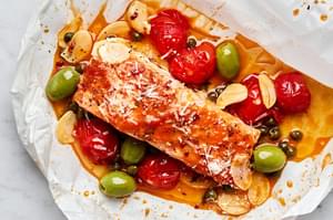A perfectly cooked salmon en papillote, served with a rich, velvety tomato butter toped with tomatoes, green olives & capers