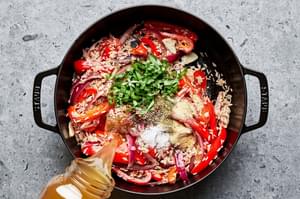 chicken stock being poured into a skillet with peppers, onions, rice and spices
