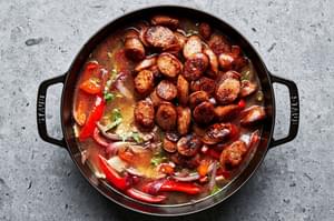 Italian sausage, chicken stock, peppers, onions, rice and spices being combined in a skillet