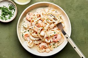 a bowl of homemade seafood fettuccine alfredo made with shrimp and scallops, sprinkled with parsley