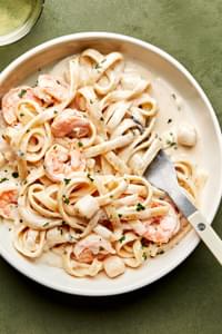 a bowl of homemade seafood fettuccine alfredo made with shrimp and scallops, sprinkled with parsley
