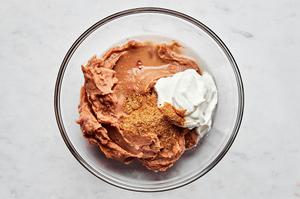 refried beans, taco seasoning and sour cream being combined in a bowl