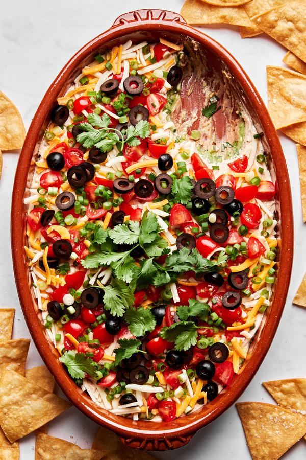 seven layer dip made with guacamole, refried beans, shredded cheese, sour cream, tomatoes, olives, green onion and cilantro