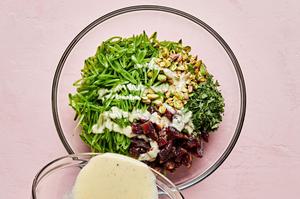 goat cheese dressing being drizzled over sliced snap peas, chopped dates, pistachios and mint leaves
