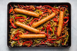 raw Italian sausage on a rimmed baking sheet with sliced onions and bell peppers