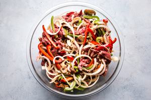 onions, bell peppers, thinly sliced steak and mushrooms in a bowl for Philly cheese steaks mixed in a bowl with marinade.