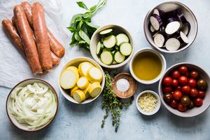 ingredients for ratatouille on a counter, zucchini, yellow squash, tomatoes, eggplant sliced, thyme, basil and sausage