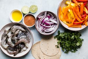 ingredients for shrimp fajitas, tortillas, cilantro, bell peppers, onions, taco seasoning, lime and olive oil