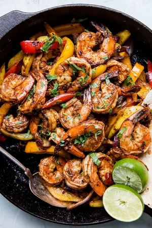 shrimp fajitas in a cast iron skillet with cilantro, limes and bell peppers