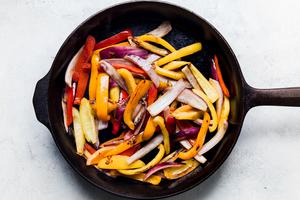 thinly sliced bell peppers and red onions in a cast iron