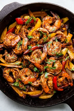 shrimp fajitas in a cast iron skillet with cilantro and bell peppers