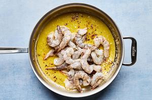 shrimp being added to a skillet with scampi sauce made with butter, olive oil, wine, garlic and spices