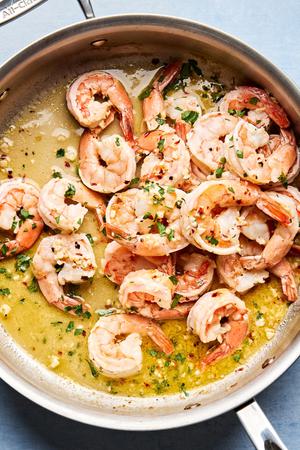 shrimp scampi in a skillet made with butter, olive oil, wine, lemon juice, parsley and spices