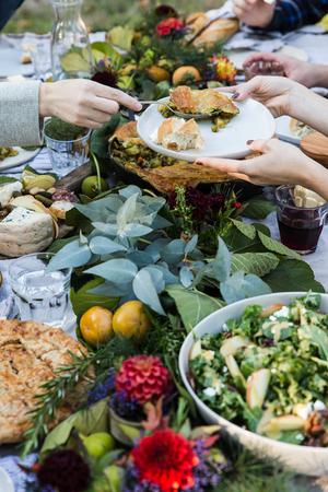 hands serving lamb pot pie to each other across the table