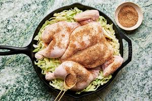 taco seasoning being robbed on a a spatchcocked chicken on top of shredded cabbage seasoned with salt in a cast iron skillet