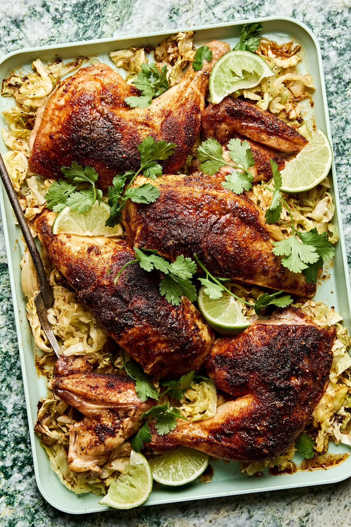 a platter of roasted chicken cut in quarters served on top of cabbage with lime wedges