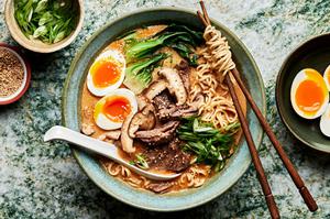 a bowl of slow cooker curry beef ramen topped with soft boiled eggs with a spoon and chopsticks