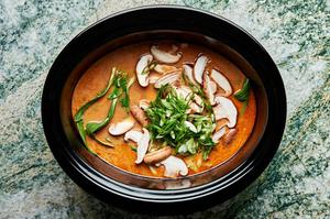 bok choy, green onions and mushrooms being added to a slow cooker with curry sauce