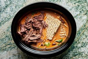 shredded beef and dried ramen being added to a slow cooker with curry sauce