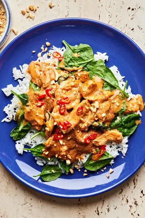 slow cooker swimming rama served on top of white rice topped with crushed peanuts, basil and red chili flakes