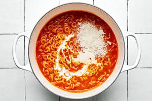 cream & Parmesan being added to a pot with tomato paste, butter, spices, tomato sauce, chicken stock