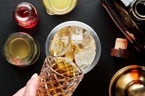 bourbon and apple cider being added to a cocktail shaker with ice to make a spiced bourbon cocktail