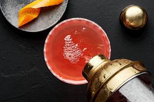 a spiced bourbon cocktail being poured out of a cocktail shaker into a coupe glass
