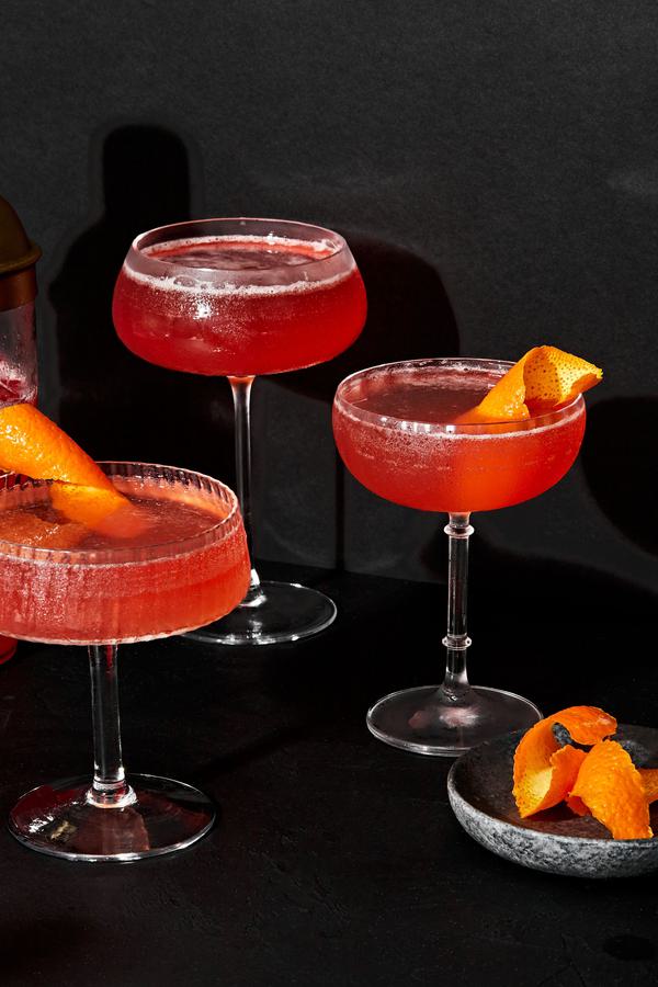 3 spiced bourbon cocktails in coupe glasses made with cranberry-orange simple syrup and garnished with an orange peel twist
