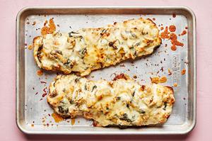 homemade spinach artichoke bread topped with melted mozzarella and parmesan on a baking sheet just out of the oven
