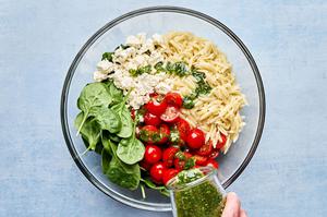 spinach, cooked orzo, tomatoes, feta and basil vinaigrette being tossed in a glass bowl