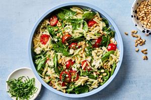 Spinach Orzo Salad With Feta Tomatoes and a Basil Dressing next to bowls of fresh basil and pine nuts for topping