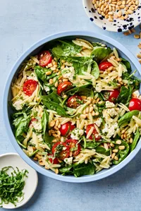 a bowl of Spinach Orzo Salad With Feta Tomatoes and a Basil Dressing topped with basil and pine nuts