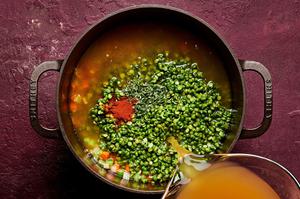 chicken stock, split peas, thyme, and paprika being added to a pot with carrots, celery and onions