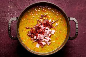ham and bacon being added to a soup pot with chicken stock, split peas, thyme, and paprika, carrots, celery and onions