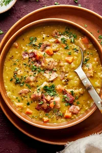 a bowl of homemade split pea soup with ham and bacon sprinkled with fresh parsley