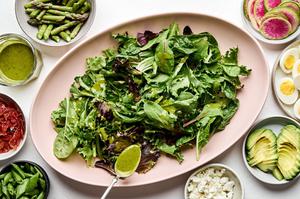 salad greens surrounded by avocado, asparagus, watermelon radish, pancetta and boiled eggs to make a spring cobb salad